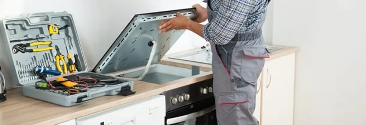 Cooktop repair technician lifting a built-in stovetop for service in New Orleans, LA