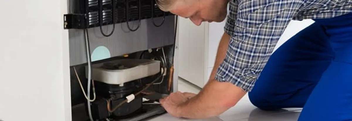 Refrigerator repair technician servicing the compressor and condenser area in New Orleans, LA